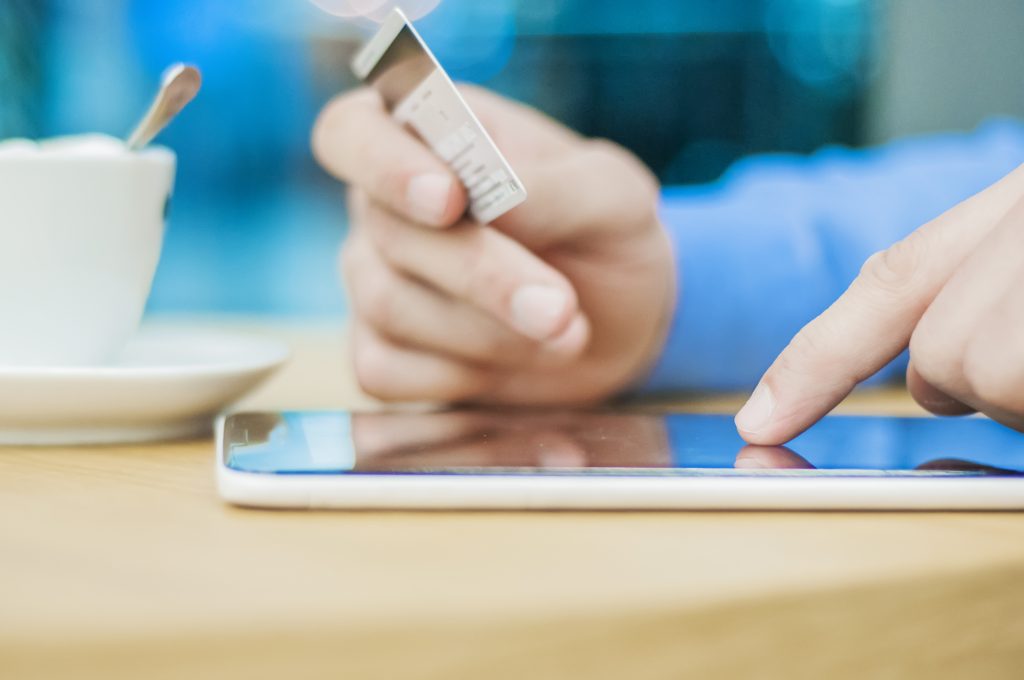 Qu’est-ce que la vérification bancaire instantanée (IBV)? - dmocredit Gros plan sur une main tenant une carte bancaire et effectuant une transaction en ligne sur une tablette, illustrant un paiement numérique ou une vérification bancaire instantanée.