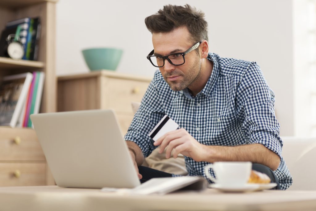 Homme concentré devant son ordinateur portable, carte bancaire à la main, comparant un prêt rapide à un prêt bancaire traditionnel en ligne.